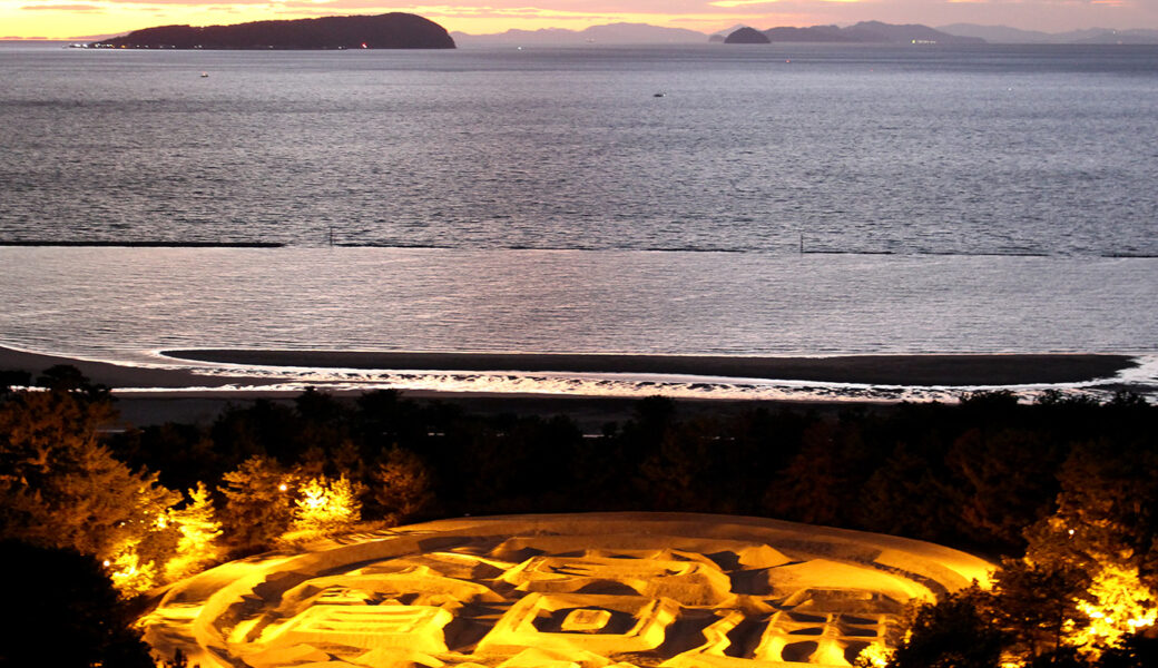 観音寺市の銭形砂絵「寛永通宝」がゴールドライトアップされる。香川の夜空に黄金の輝きを